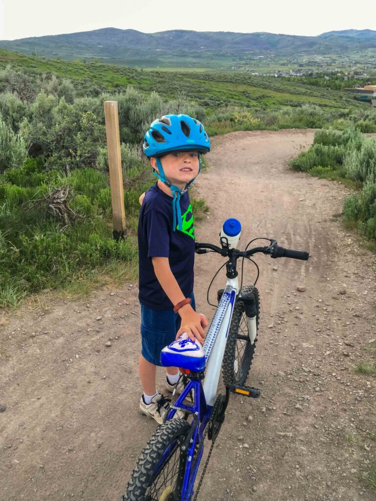 kid wearing a kids bike helmet standing beside his mountain bike