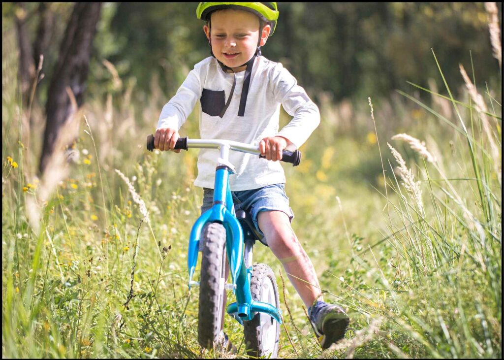 a 5year old boy wearing a yellow helmet riding his balance bike through a field