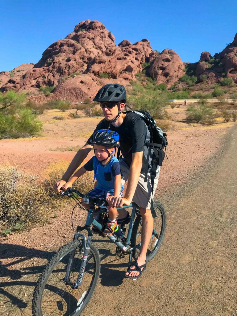 a dad riding a bike on a mountain trail with his son sitting on a front-mounted kids bike seat