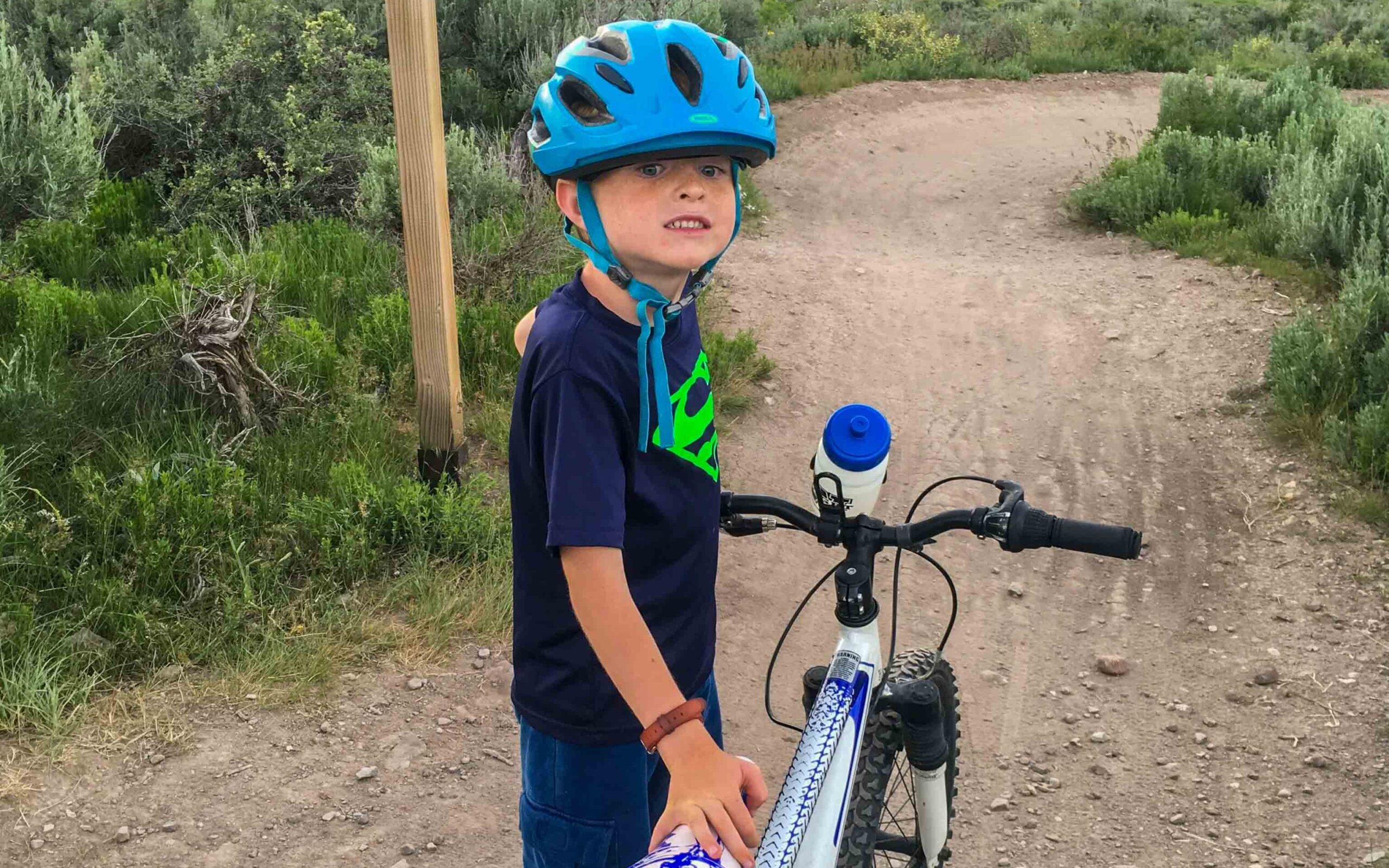 kid wearing a kids bike helmet standing beside his mountain bike